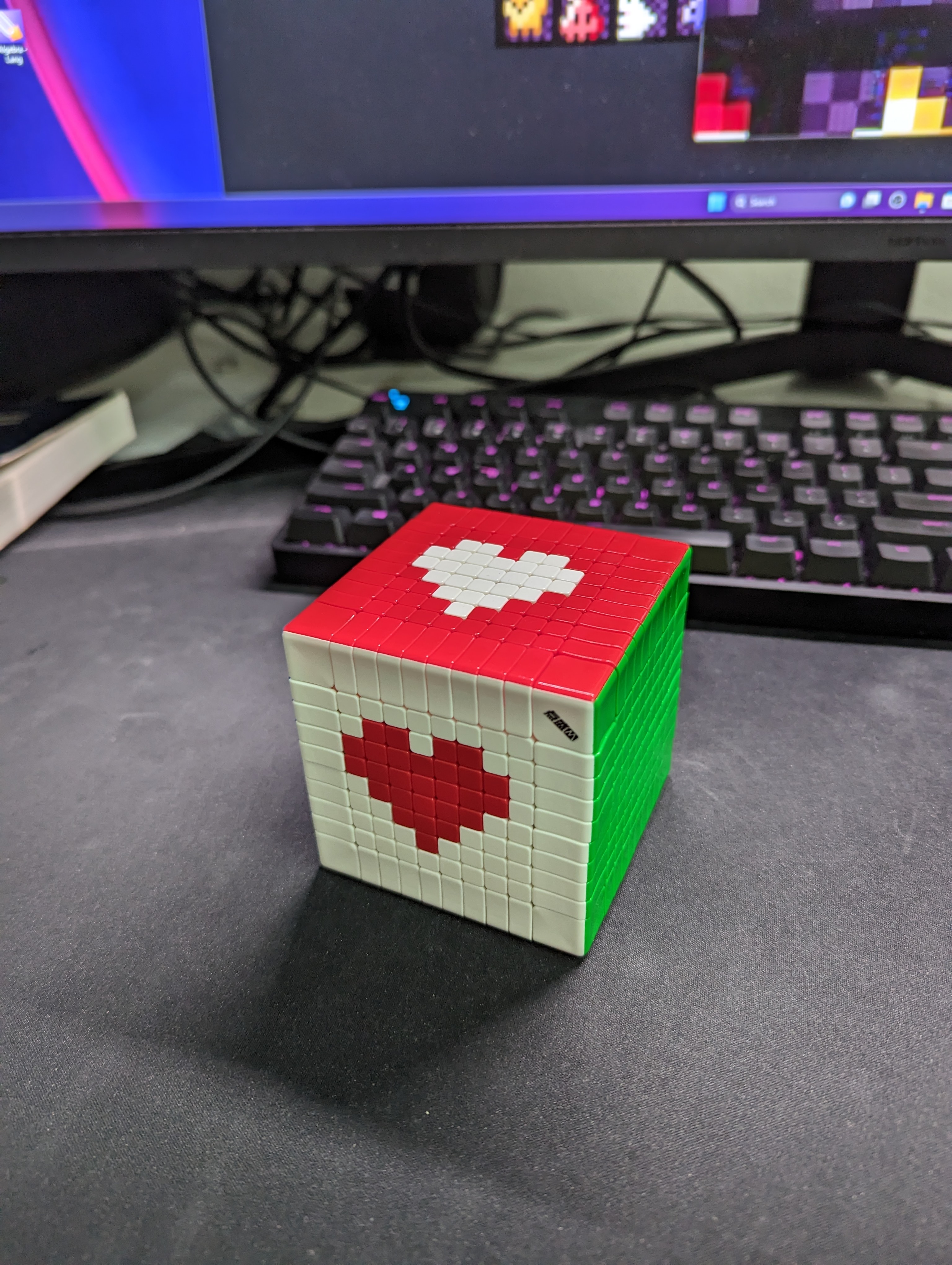 A cube on a desk with a red heart on its white front face and a white heart on its red top face.