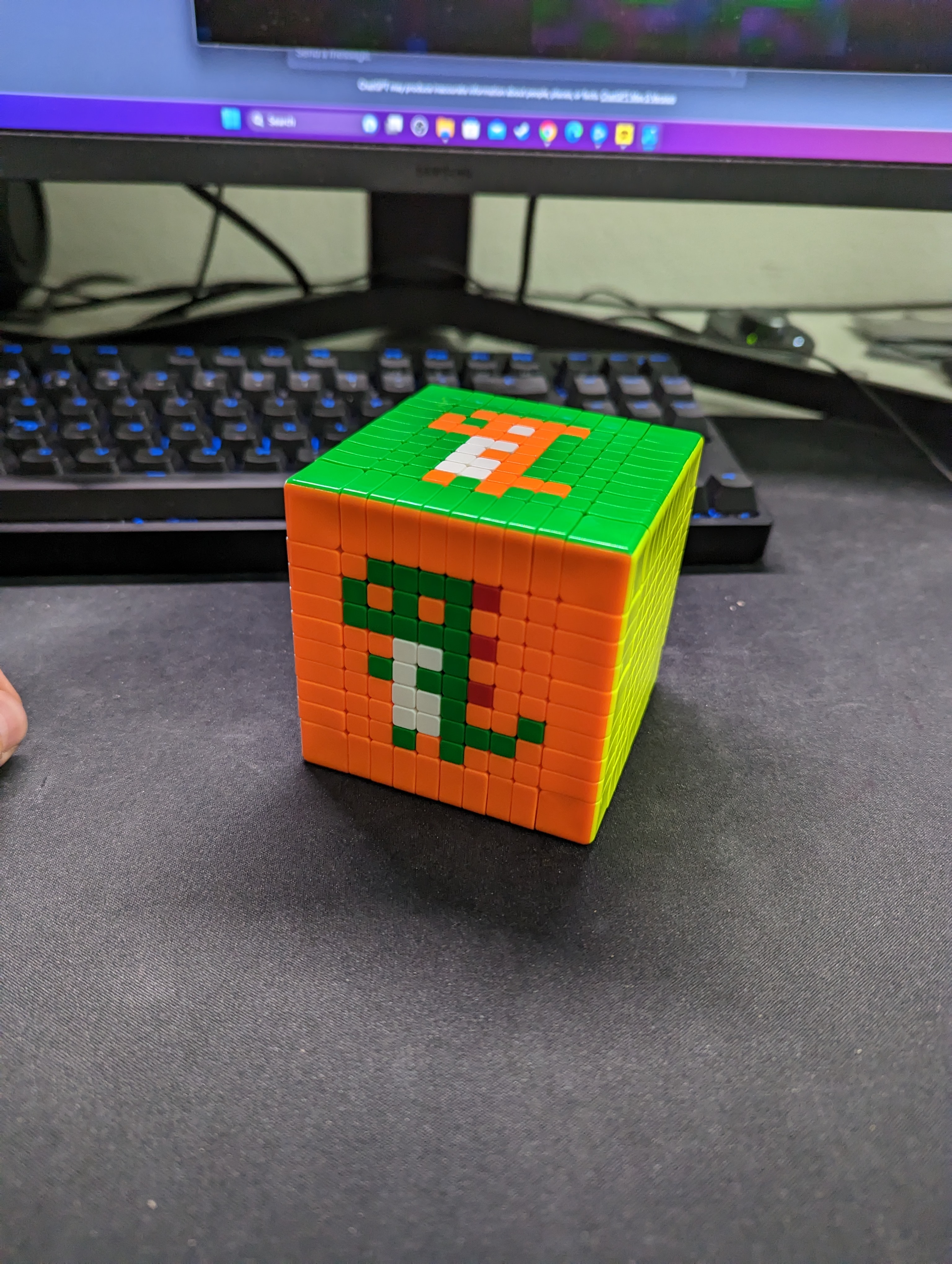 A cube with a green pixel figure on its orange front face and an orange pixel figure on its green top face, both with white details.